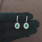 Load and play video in Gallery viewer, Video showcasing the 0.85 CT natural round cut diamond hoop earrings with a central oval green colourstone, set in 18kt white gold. Highlighting the elegant blend of sparkling diamonds and the striking green stone in motion.
